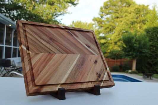 Wooden cutting board with a geometric pattern on a stand outdoors.