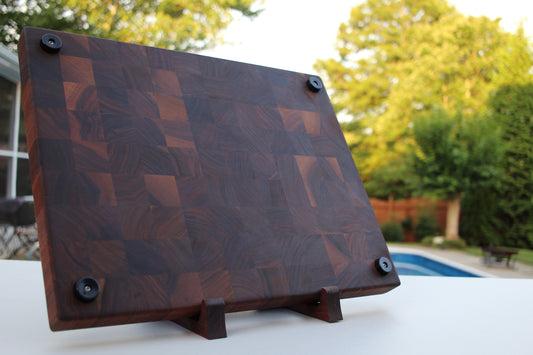 End Grain Walnut Wooden cutting board with a geometric pattern on a stand outdoors.