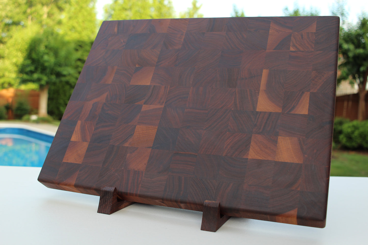End Grain Walnut Wooden cutting board with a geometric pattern on a stand outdoors.